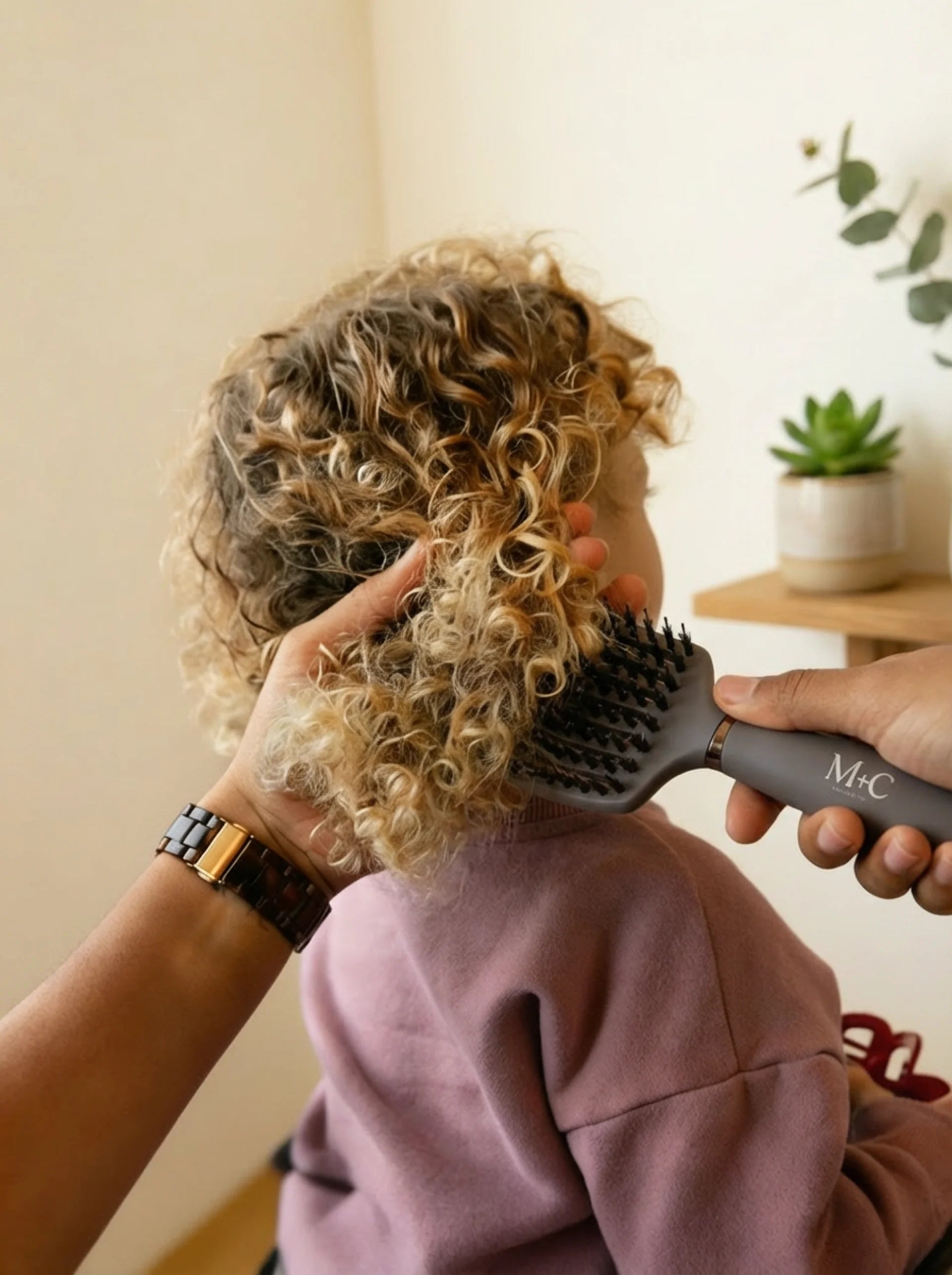 Close-up of a young girl with curly hair being gently detangled using the M + C Collective Ultimate Detangler brush